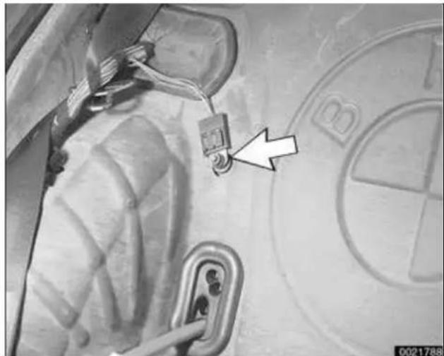 Close-up of a car door panel with a small electronic component and a white arrow pointing to a detail, against a blurred background with a BMW logo (no readable text or symbols)