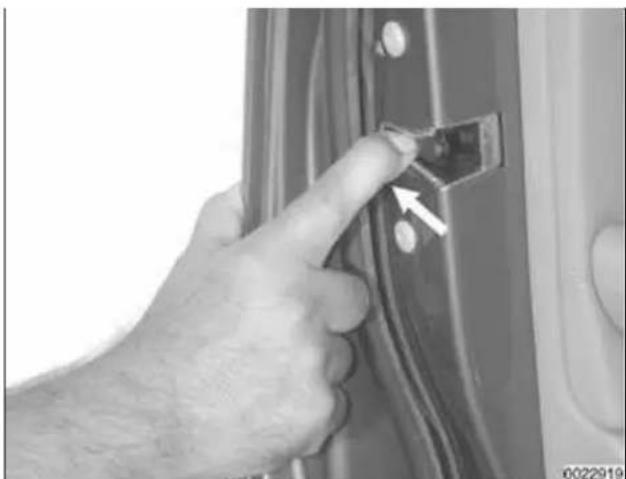 Close-up of a hand inserting a small component into a door panel, with an arrow pointing to the component (no text or symbols visible)