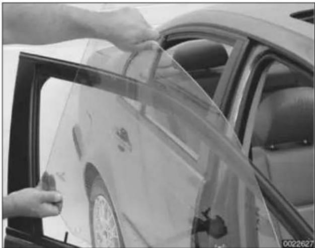 Person cleaning a car window with a plastic wrap (no visible text or symbols)