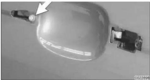 Close-up of a mechanical component with a white arrow pointing to a small circular feature (no visible text or symbols)