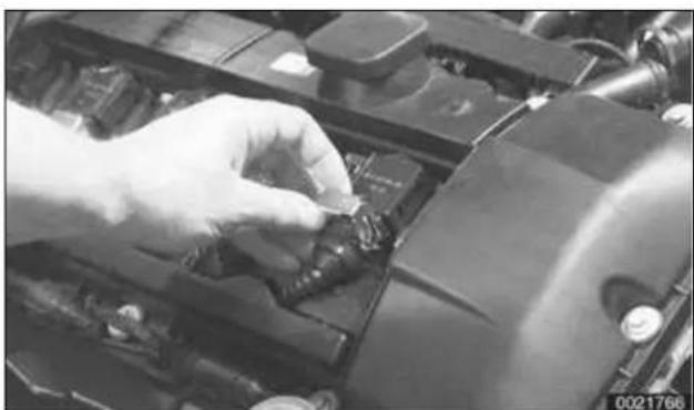Close-up of a gloved hand adjusting a small component on an engine compartment (no visible text or symbols)