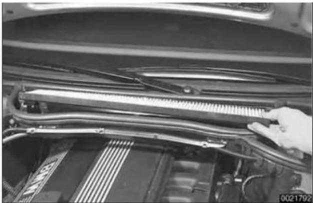 Close-up of a car engine bay with visible internal components and a hand adjusting the handle (no text or symbols)
