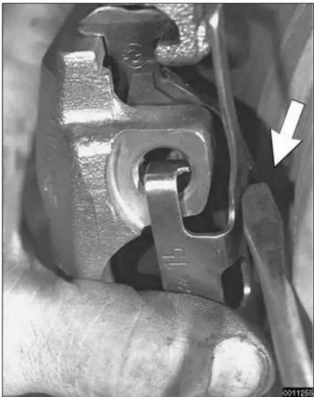 Close-up of a mechanical clamp or bracket component being held, with a white arrow pointing to a specific part (no text or symbols visible)