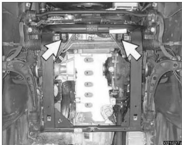 Undercarriage view of a vehicle chassis with visible structural components and two white arrows pointing to specific parts (no text or symbols present)