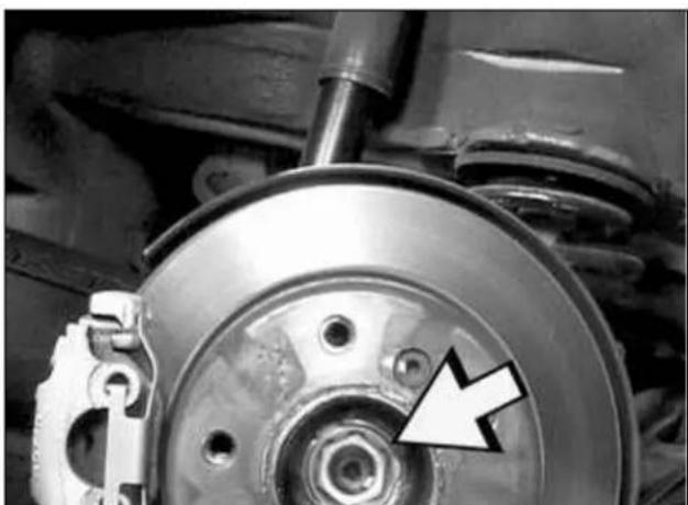 Close-up of a car brake system with a circular component and a white arrow pointing to a bolt (no text or symbols visible)