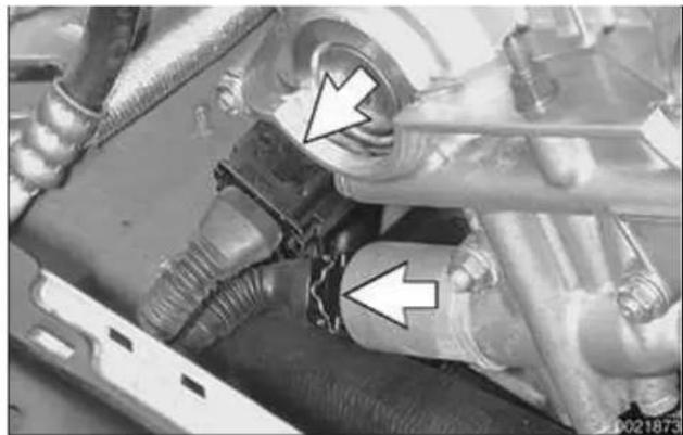 Close-up of an automotive engine component with two white arrows pointing to specific parts (no visible text or symbols)