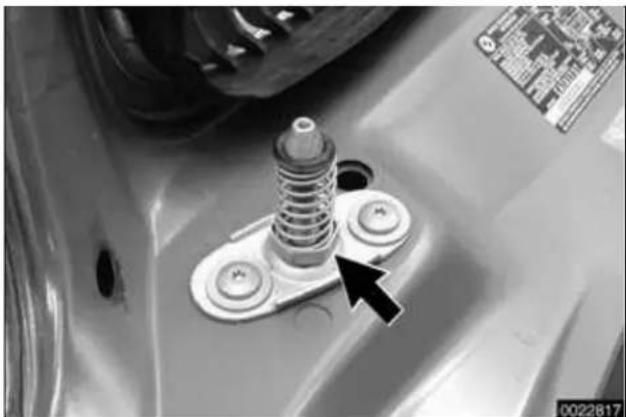 Close-up of a mechanical component with a spring and mounting base, featuring a black arrow pointing to a bolt (no visible text or symbols)