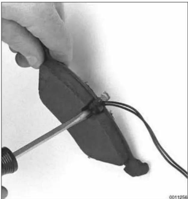 Close-up of a hand using a screwdriver to cut a black mechanical component with wires (no visible text or symbols)