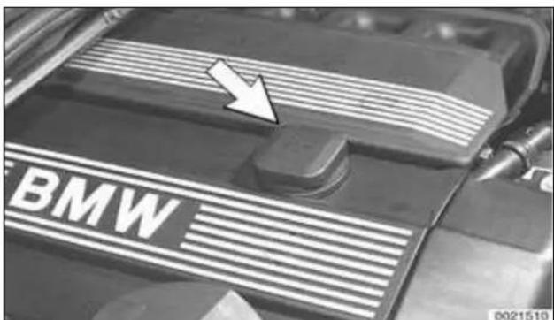 Close-up of a BMW engine bay with a white arrow pointing to the side panel (no text or symbols on the body)