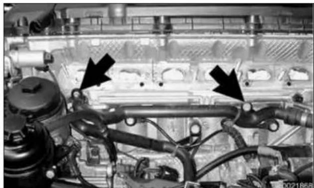 Close-up of an engine cylinder head with visible internal components and two black arrows pointing to specific parts (no text or symbols present)