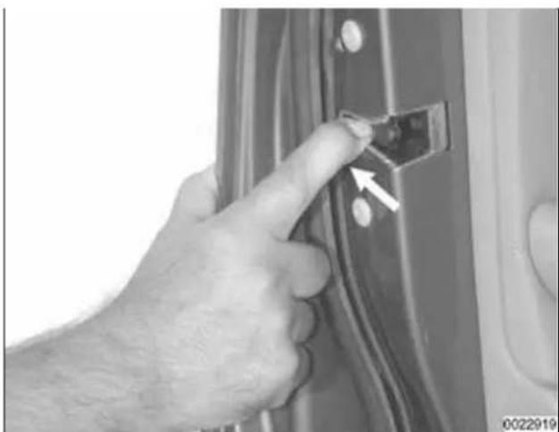 Close-up of a hand inserting a small component into a car door panel, with an arrow pointing to the component (no text or symbols visible)