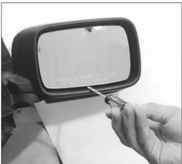 Close-up of a hand using a screwdriver to apply a mirror on a car side mirror (no visible text or symbols)