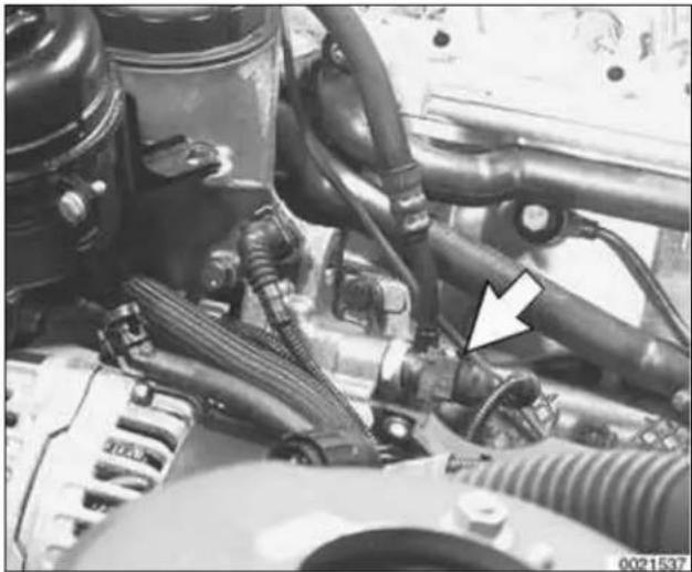 Close-up of an automotive engine bay with hoses and a white arrow pointing to a component (no visible text or symbols)