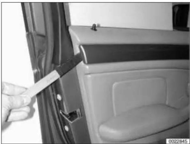 Close-up of a hand holding a white strip attached to a car door, showing interior compartments and a small object on the door (no visible text or symbols)