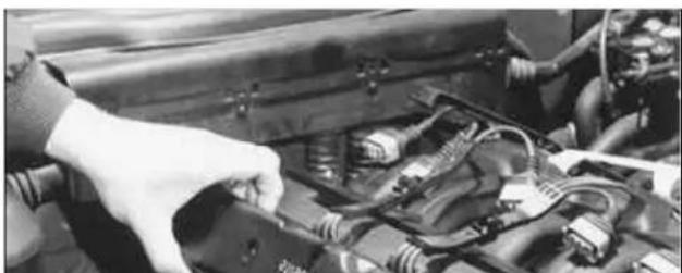 Close-up of a hand adjusting the engine compartment with visible wiring and components (no text or symbols)