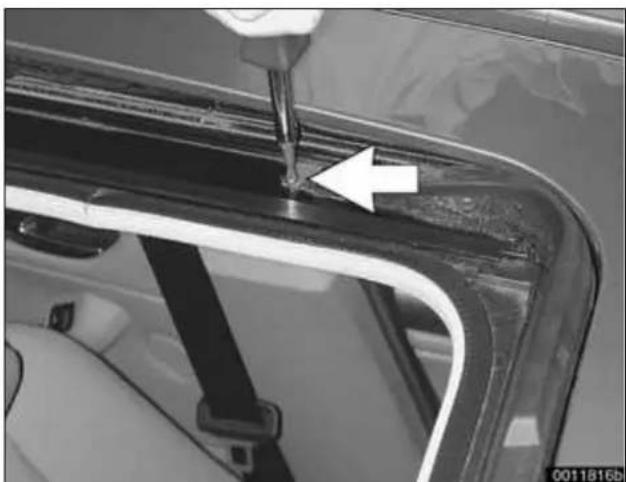 Close-up of a car's door panel with a screwdriver inserted, showing a white arrow pointing to a seam or defect (no text or symbols visible)