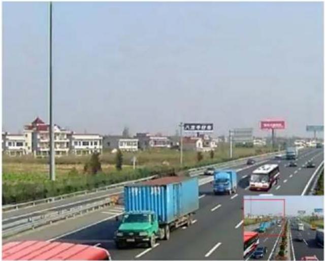 Highway scene with vehicles and trucks, residential buildings in background (no visible text or symbols)