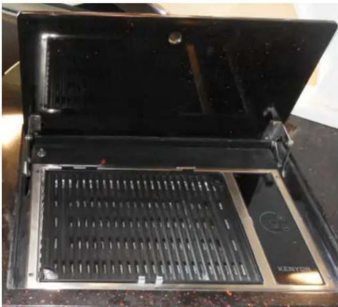 Open kitchen appliance with black tray and metal grating, no visible text or symbols on the main body