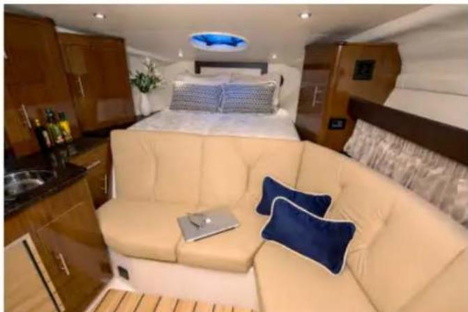 Interior view of a modern luxury car cabin featuring a beige sofa, cream-colored bedding, and a blue pillow (no visible text or symbols)