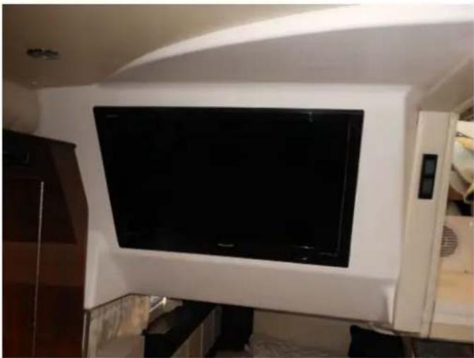 Interior view of a modern living room with a large black TV mounted on a white wall (no visible text or symbols)