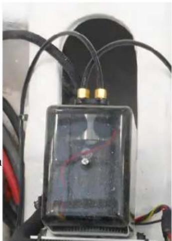 Close-up of a black rectangular electronic device with gold connectors and wires, mounted on a white surface (no visible text or symbols)