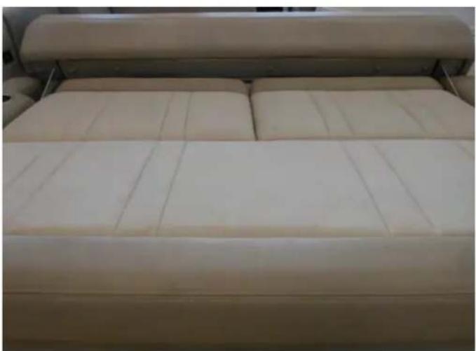 Top-down view of a beige bed with two pillows and a rolled-up blanket (no text or symbols visible)