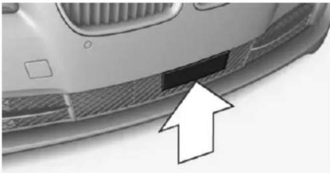 Close-up of a car's front bumper with a black rectangular patch and an arrow pointing to it (no text or symbols visible)