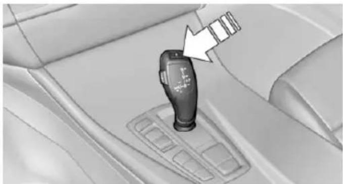 Interior view of a car gear shift lever with a white arrow pointing to the handle (no text or symbols visible)
