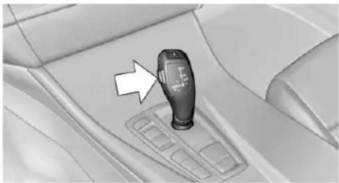 Interior view of a car gear shift lever with a white arrow pointing to the mode (no text or symbols visible)