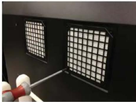 Close-up of a black ventilation grille with grid patterns and a red tool inserted, no visible text or symbols