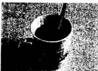 Schwarz-Weiß-Foto einer kleinen Schüssel mit einem Löffel, möglicherweise einer Tasse oder einem Behälter, vor einem strukturierten Hintergrund (kein sichtbarer Text oder Symbole)