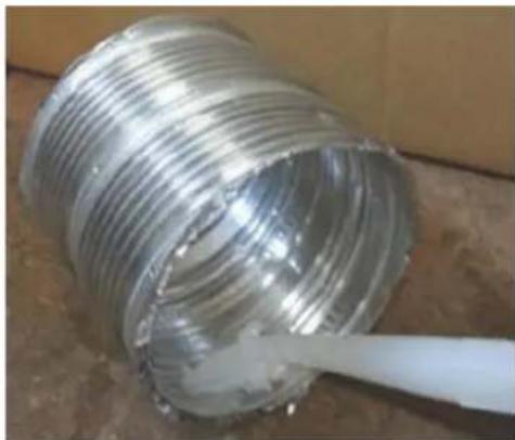 Close-up of a coiled metallic pipe with a white tool inserted, placed on a wooden surface (no text or symbols visible)