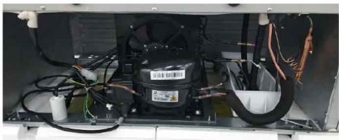 Interior view of an appliance showing internal components like a black compressor, wiring, and tubing (no visible text or symbols)