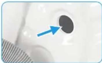 Close-up of a white object with a dark circular hole and a blue arrow pointing to it, partially overlaid by a striped pattern (no text or symbols)
