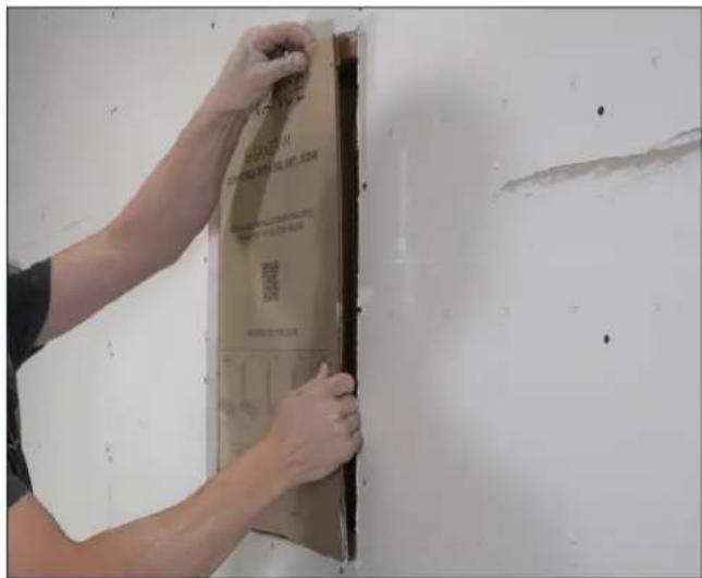 Person installing a wall-mounted label with QR code and printed text, likely for construction or repair purposes.