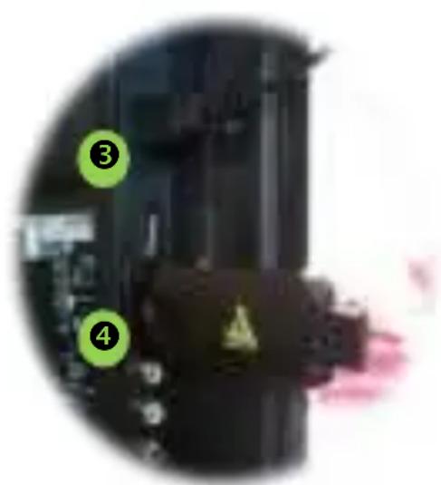 Cropped image showing numbered green circles and a black mechanical component with a warning symbol, likely from an industrial or manufacturing context.