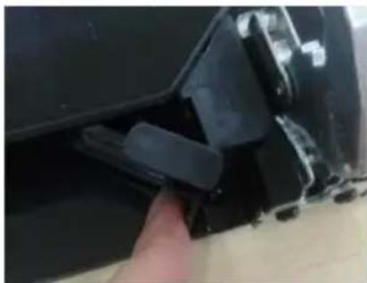 Close-up of a black plastic clip attached to a wooden frame, with a finger pointing to the edge (no text or symbols visible)