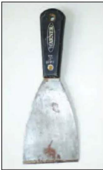 Close-up of a metal spatula with a black handle and label 'WARNER' on top (no other text or symbols visible)