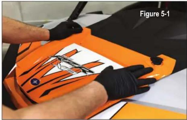 Person in gloves handling an orange car body with a white patterned design, no visible text or symbols on the object itself.
