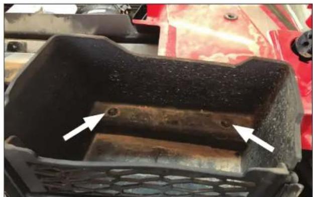 Close-up of a metal component with two white arrows pointing to a raised bolt, next to a red vehicle (no text or symbols visible)