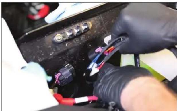 Close-up of gloved hands installing or adjusting a black automotive electrical plug with wires (no visible text or symbols)