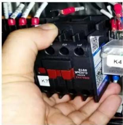 Close-up of a hand holding an electrical contactor with visible labels and QR code, likely for testing or maintenance.