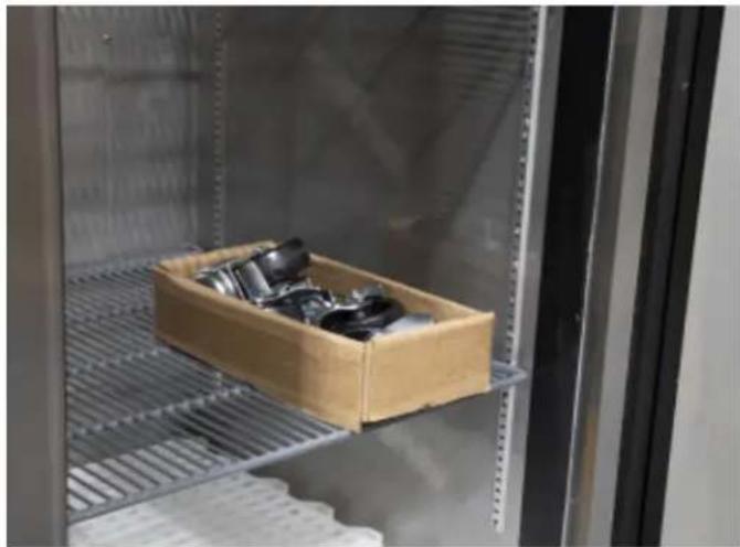 Interior view of a stainless steel storage cabinet with a wooden crate containing black plastic items, no visible text or symbols.