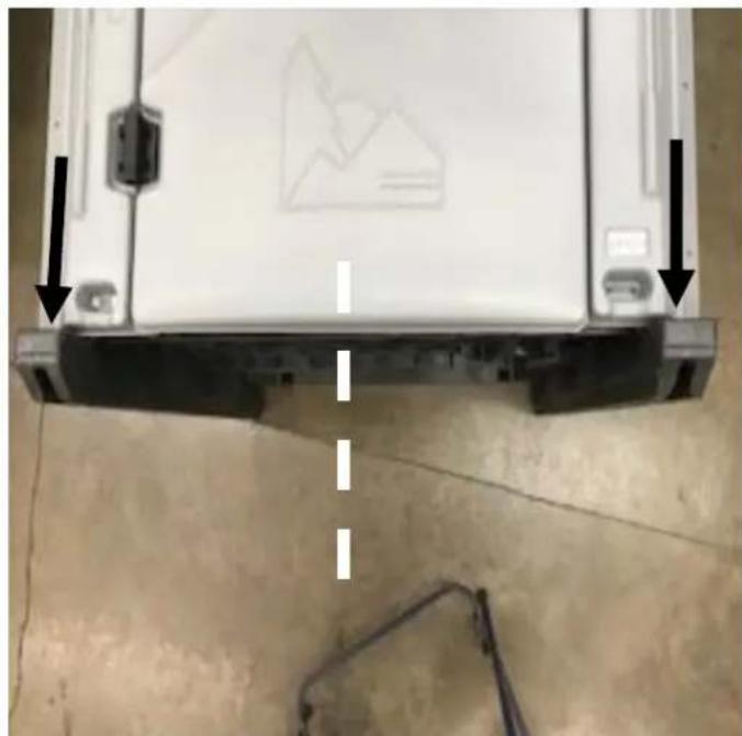 Close-up of a white electronic device with black arrows pointing to its side panel, against a concrete floor (no visible text or symbols)