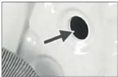 Close-up of a circular object with a black dot and an arrow pointing to it, next to a striped surface (no text or symbols visible)