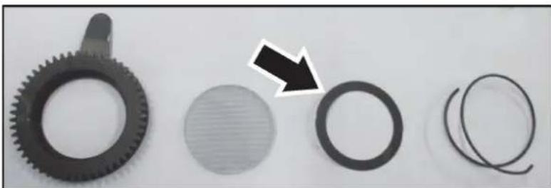 Close-up of mechanical components including a gear, a circular component with a striped pattern, and two coiled springs (no text or symbols visible)