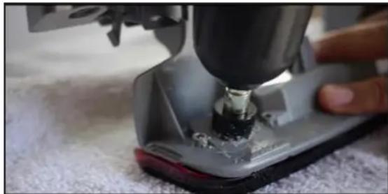 Close-up of a sewing machine needle stitching fabric, with a hand operating it (no visible text or symbols)