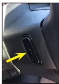 Close-up of a car interior showing a black handle and a yellow arrow pointing to a button (no text or symbols visible)