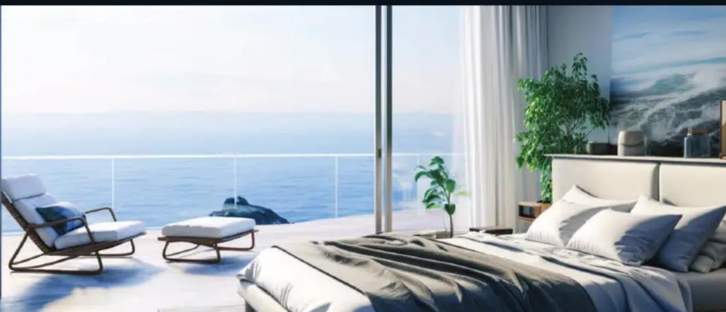 Modern bedroom interior with large window overlooking the sea, featuring a bed, lounge chairs, and potted plants (no text or symbols visible)