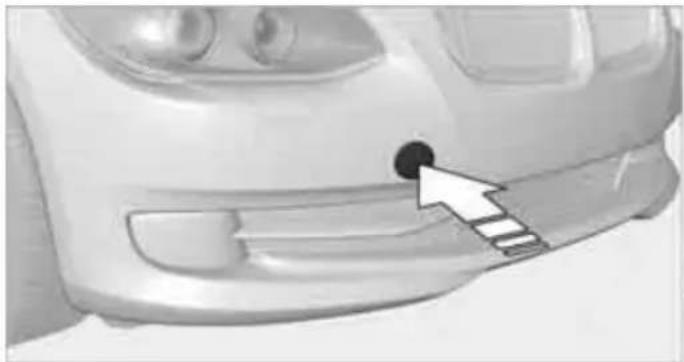 Close-up of a car's front bumper with a black circular mark and arrow pointing to the grille (no text or symbols visible)